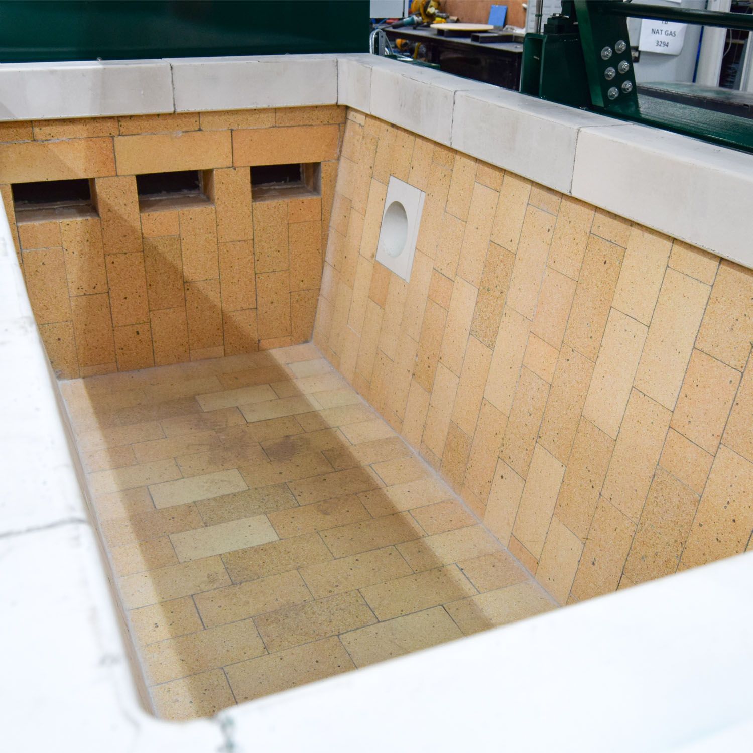 Inside the primary chamber: interlocking firebrick, the burner port in the side wall, and the pre-cast rim that takes the impact of loading.