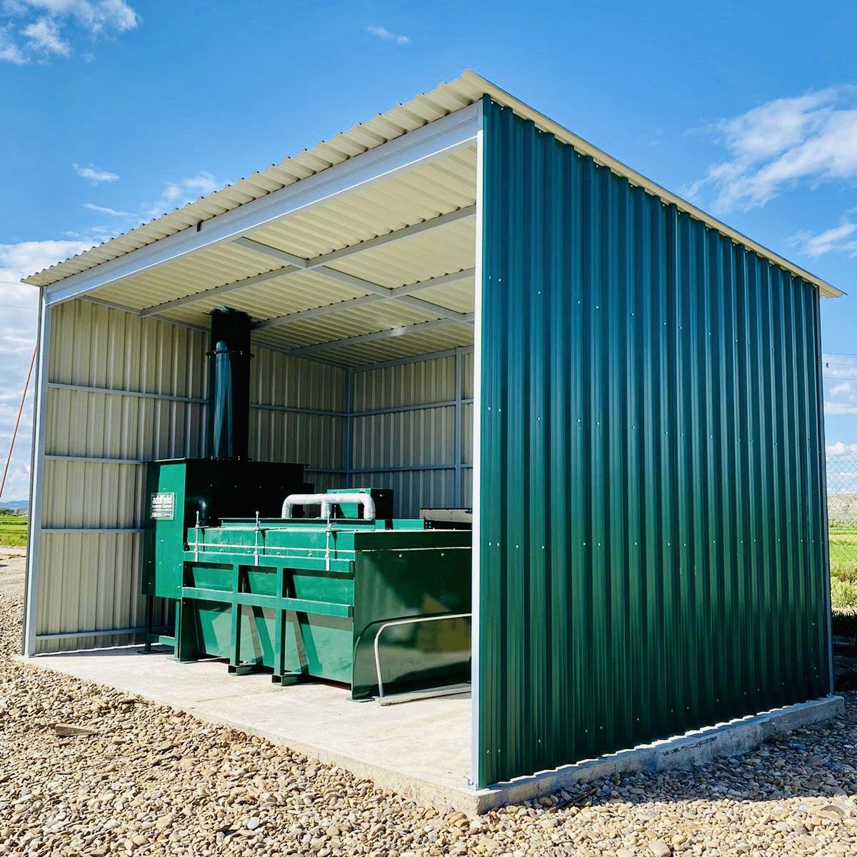 A TB installed on a concrete pad under an open-sided weather shelter, with the stack carried through the roof.